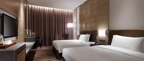 Habitación de hotel con dos camas, un escritorio, un televisor de pantalla plana, una silla y un ventanal con cortinas.