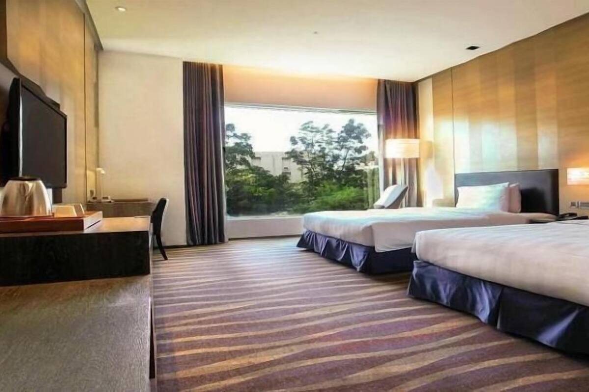 A hotel room with two beds, a desk, a TV, and a window with curtains.