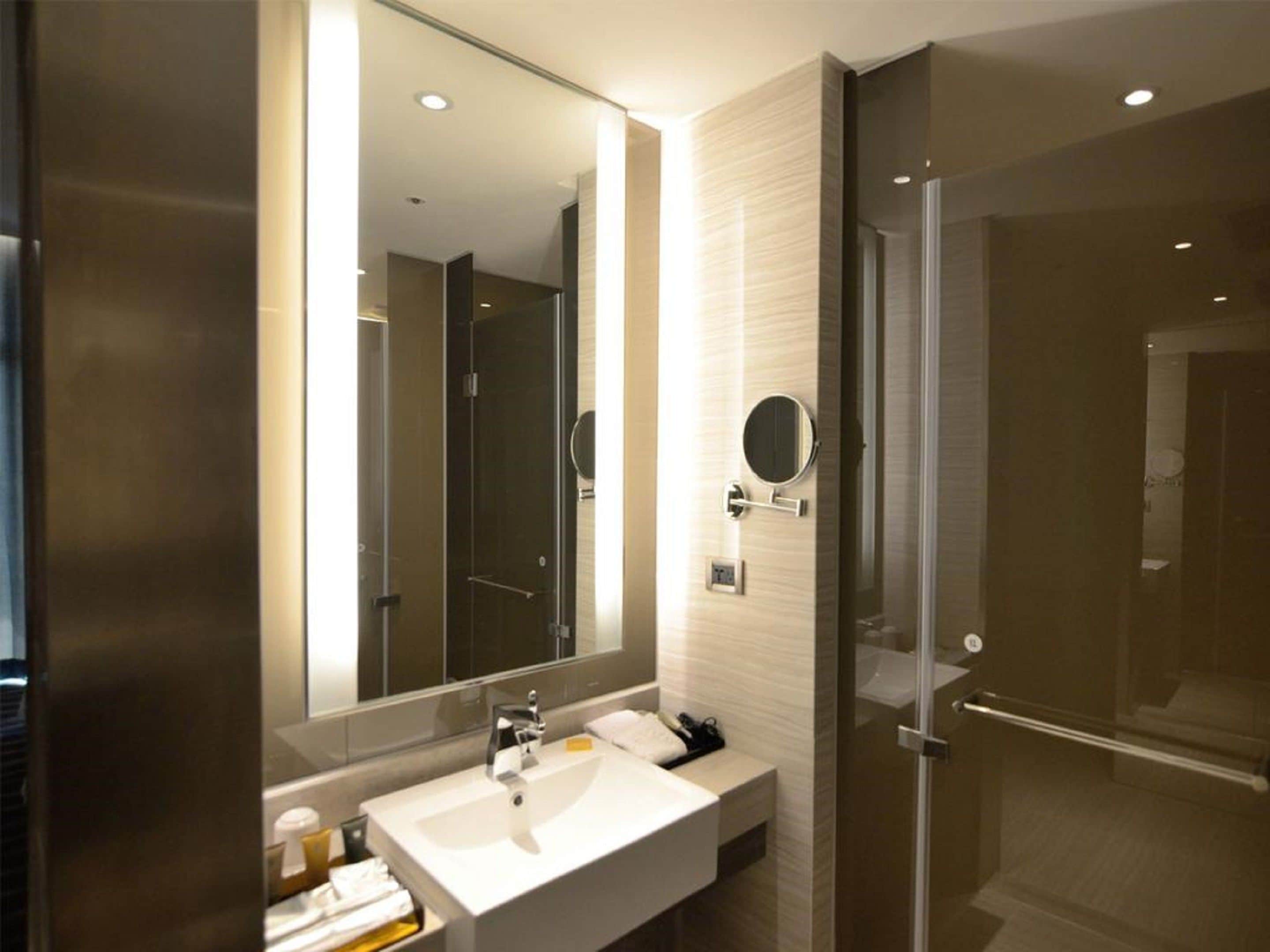 Un baño moderno con un espejo grande, un lavabo y una puerta de ducha de vidrio.