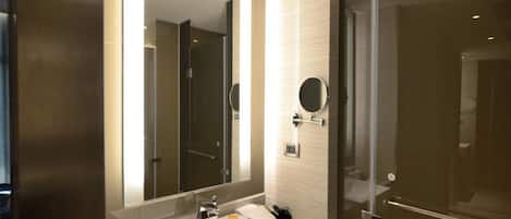 Un baño moderno con un espejo grande, un lavabo y una puerta de ducha de vidrio.