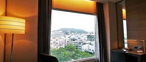 Une chambre d’hôtel avec une grande fenêtre, un bureau avec une chaise et une lampe.
