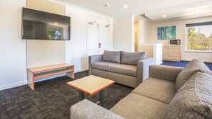 Una sala de estar moderna con televisor de pantalla plana, un sofá, una mesa de centro y una pequeña cocina con microondas.