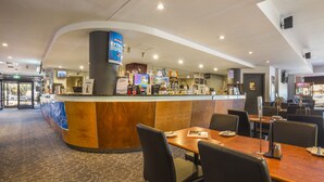 Un vestíbulo de hotel con un mostrador de recepción curvo, zona de estar y diversas comodidades, incluyendo una máquina de café y un letrero de vinos.