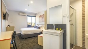 Una habitación de hotel moderna con una cama, un escritorio, un baño con ducha y un televisor montado en la pared.