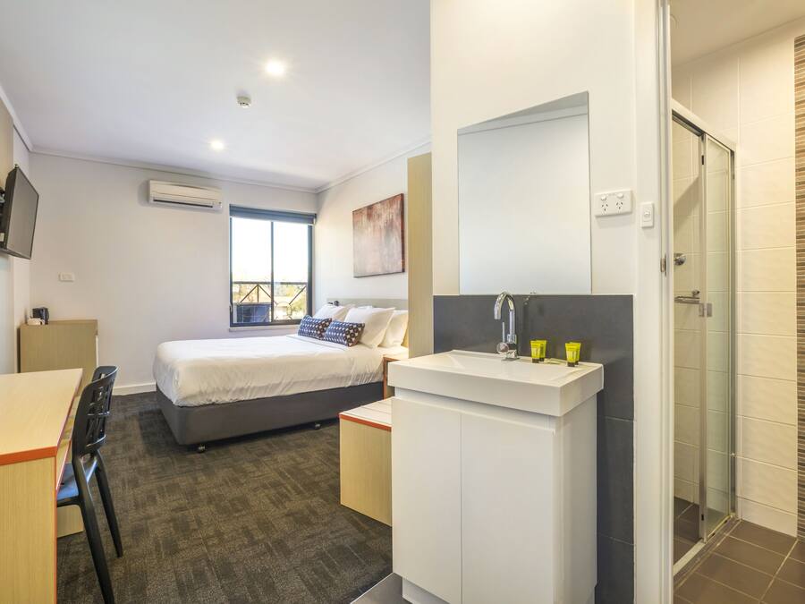 A modern hotel room with a bed, a desk, a bathroom with a shower, and a TV mounted on the wall.
