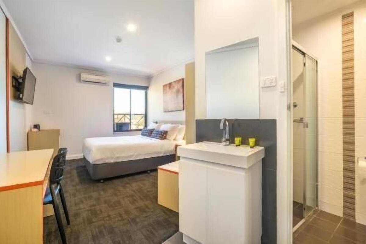 Ein Hotelzimmer mit Bett, Schreibtisch, Spiegel und Dusche.