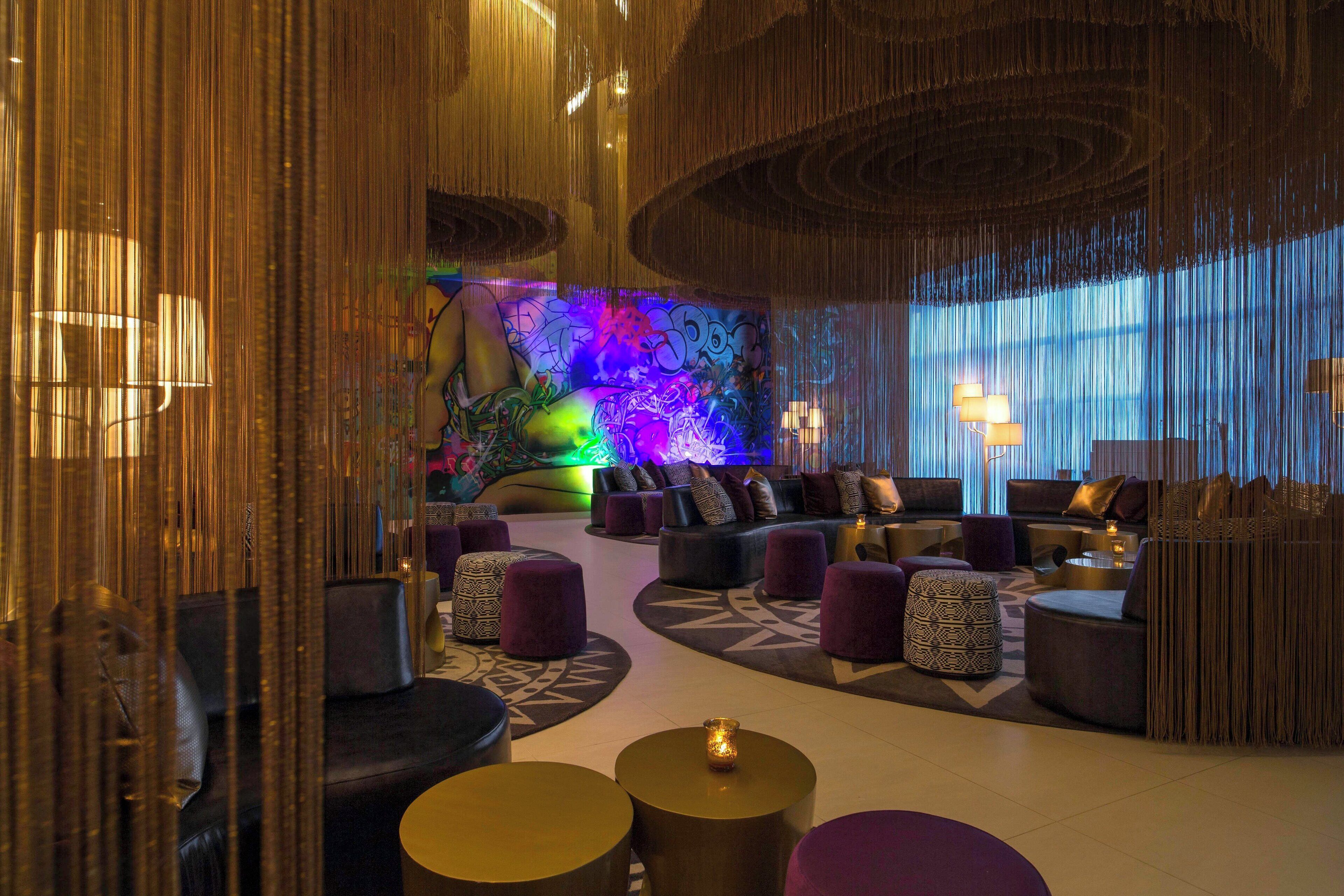 A modern lounge area with sofas, ottomans, and a colorful mural in the background.