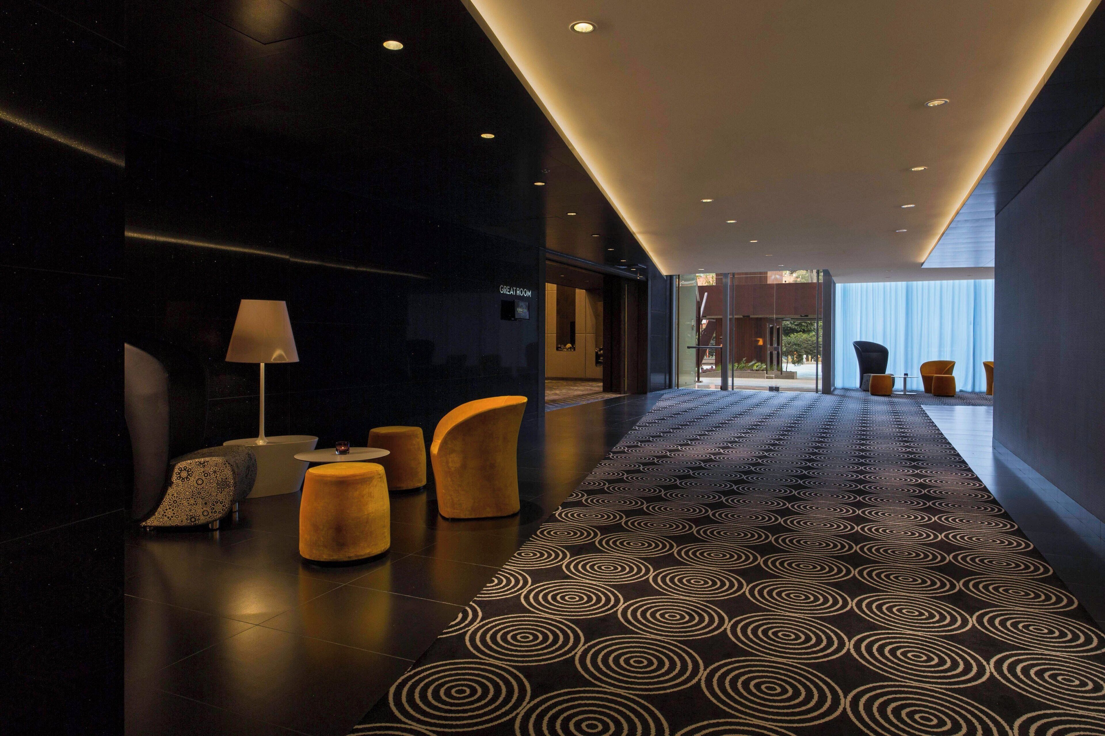 A modern lobby with a patterned carpet, seating area, and a view to a room labeled "GREAT ROOM".