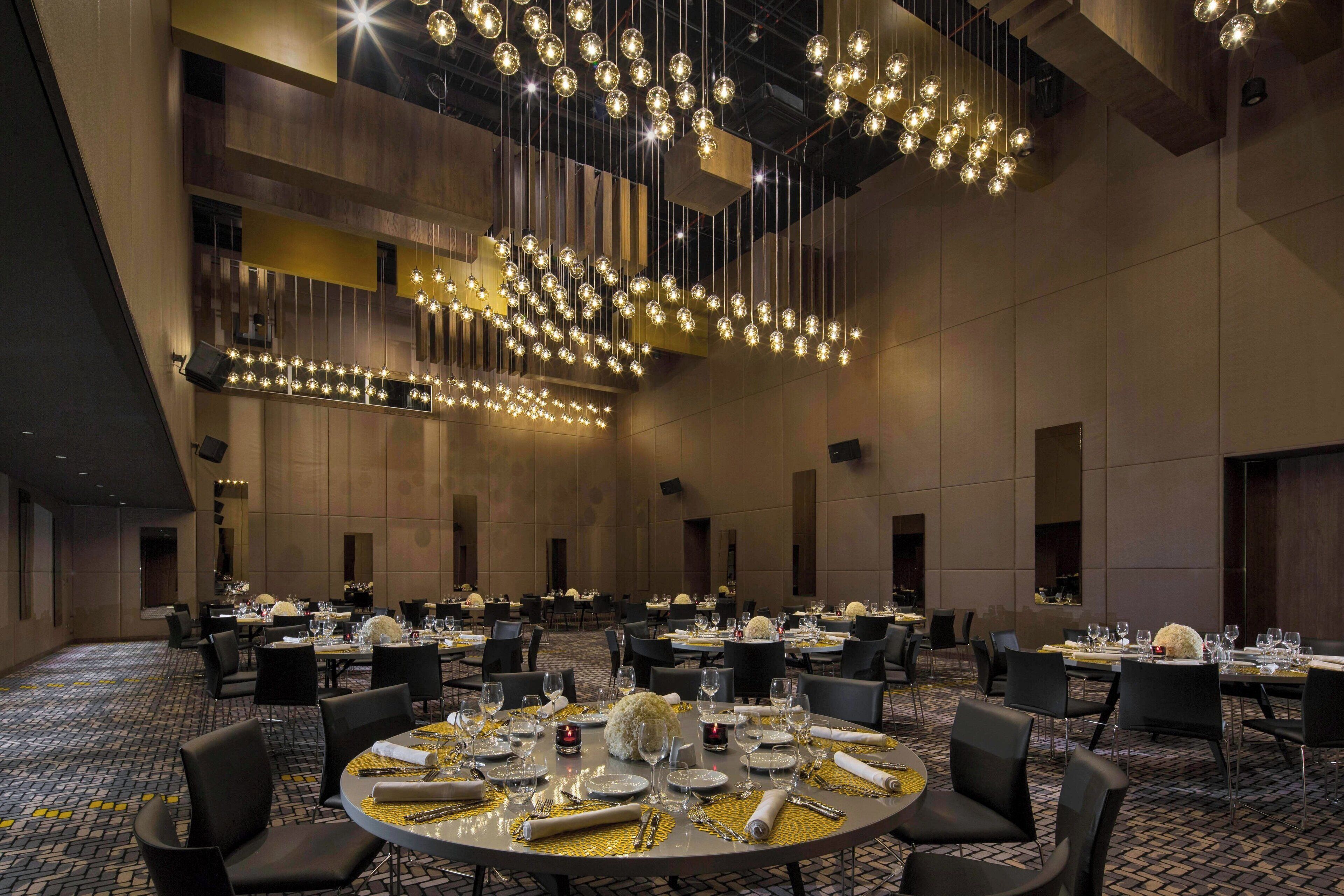 A spacious banquet hall with multiple round tables set for dining, featuring elegant table settings and a modern chandelier.