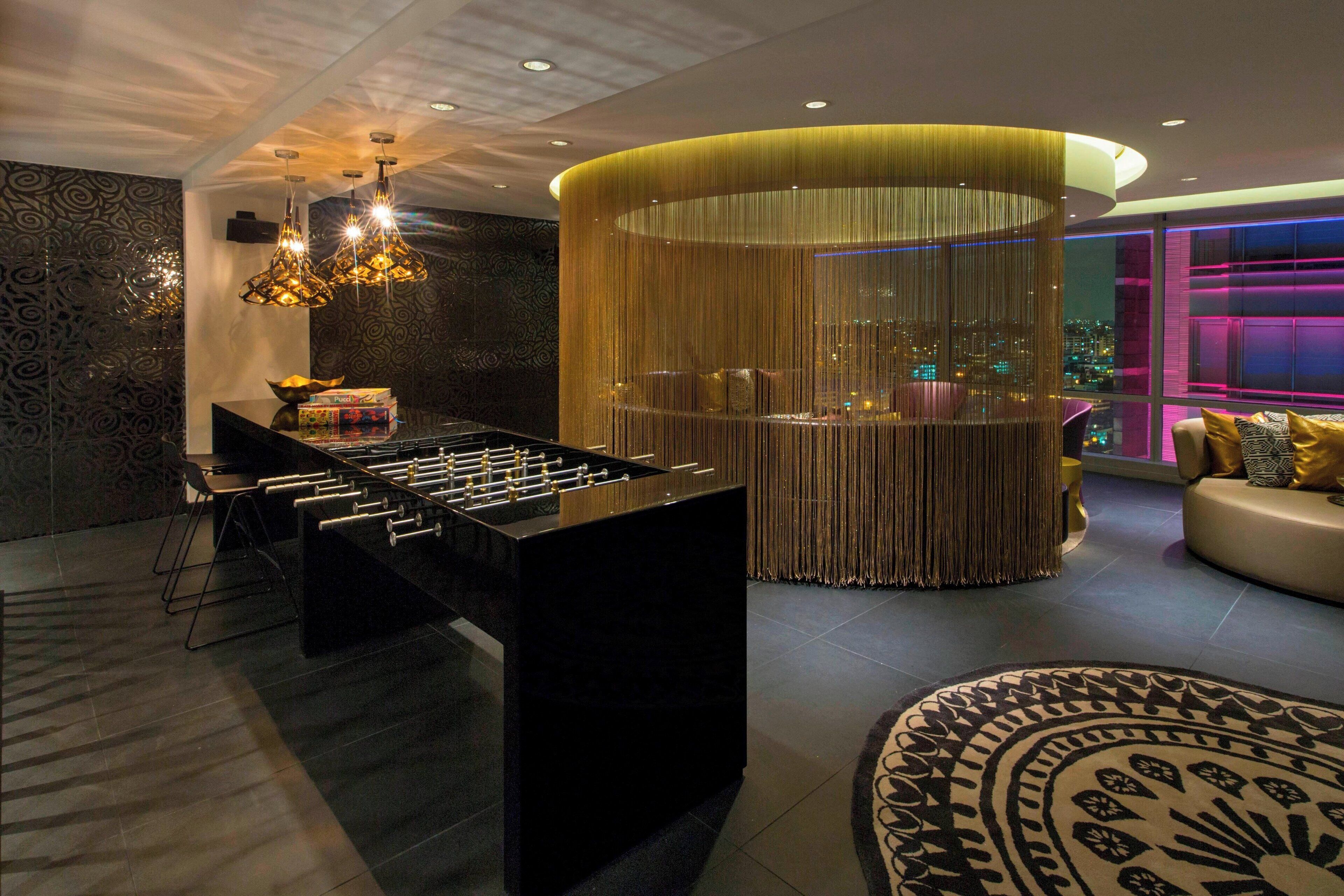 A modern interior with a foosball table, a seating area with a sofa and chairs, and a view of the city at night.