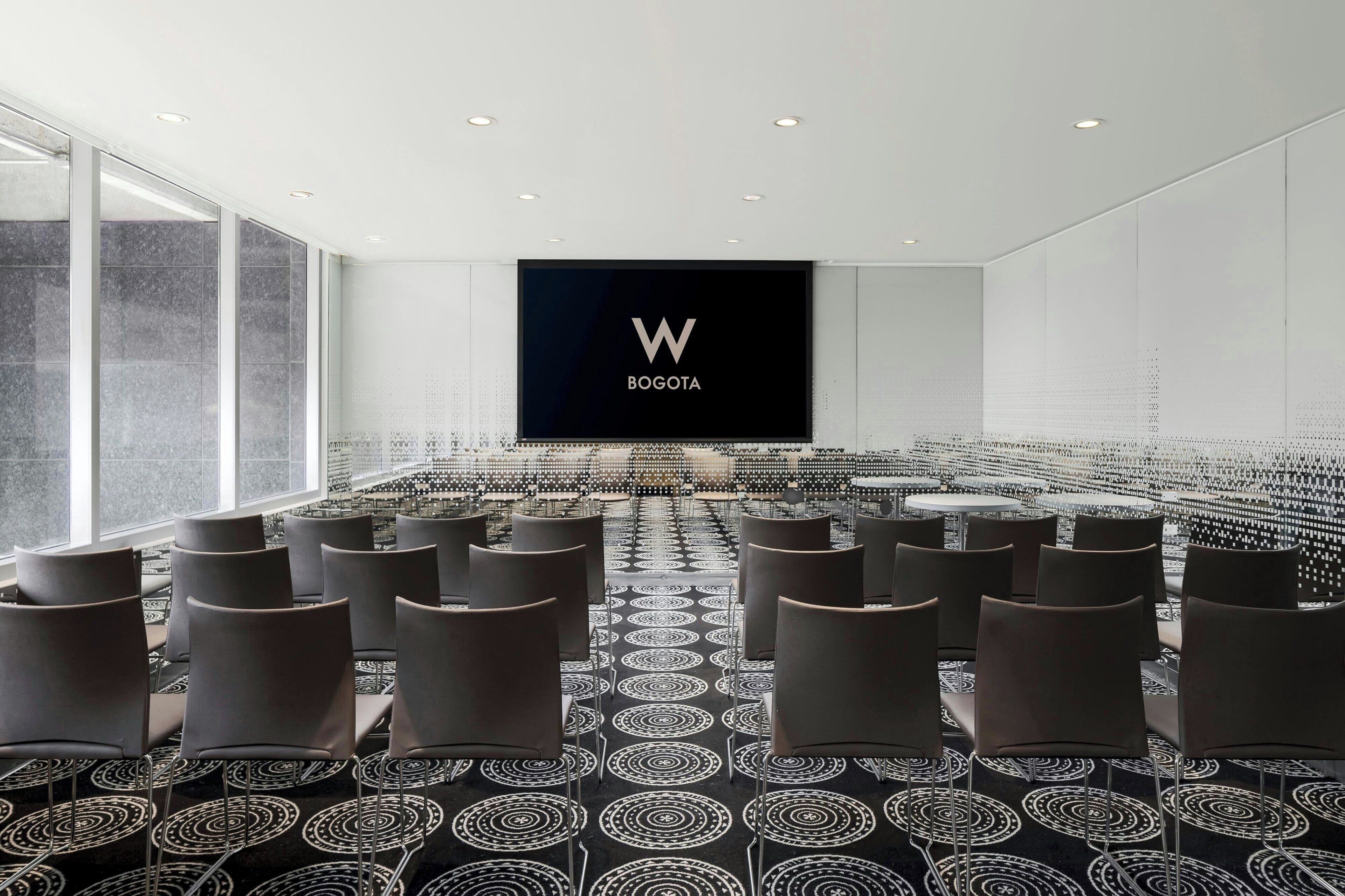A conference room with a large screen displaying "BOGOTA" and rows of chairs arranged for a meeting.