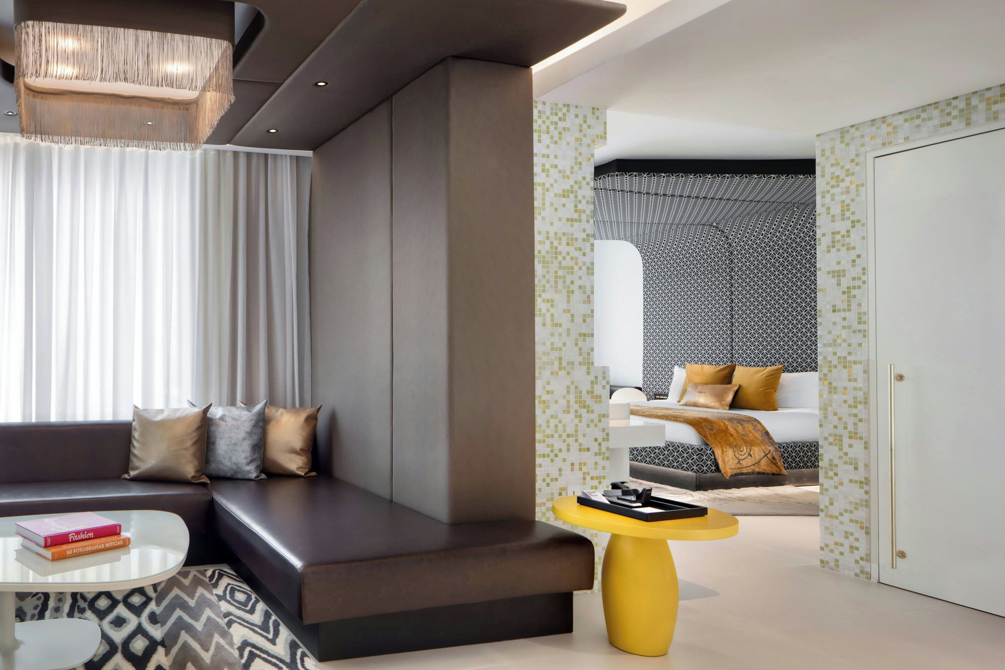 A modern hotel room with a sofa, a coffee table, a small yellow side table, and a patterned rug.