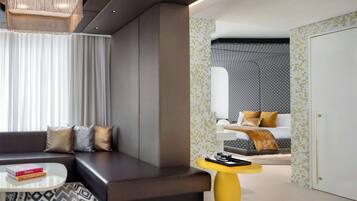 A modern hotel room with a sofa, a coffee table, a small yellow side table, and a patterned rug.