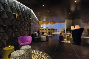 A modern lounge area with a geometric wall design, seating arrangements, and ambient lighting.
