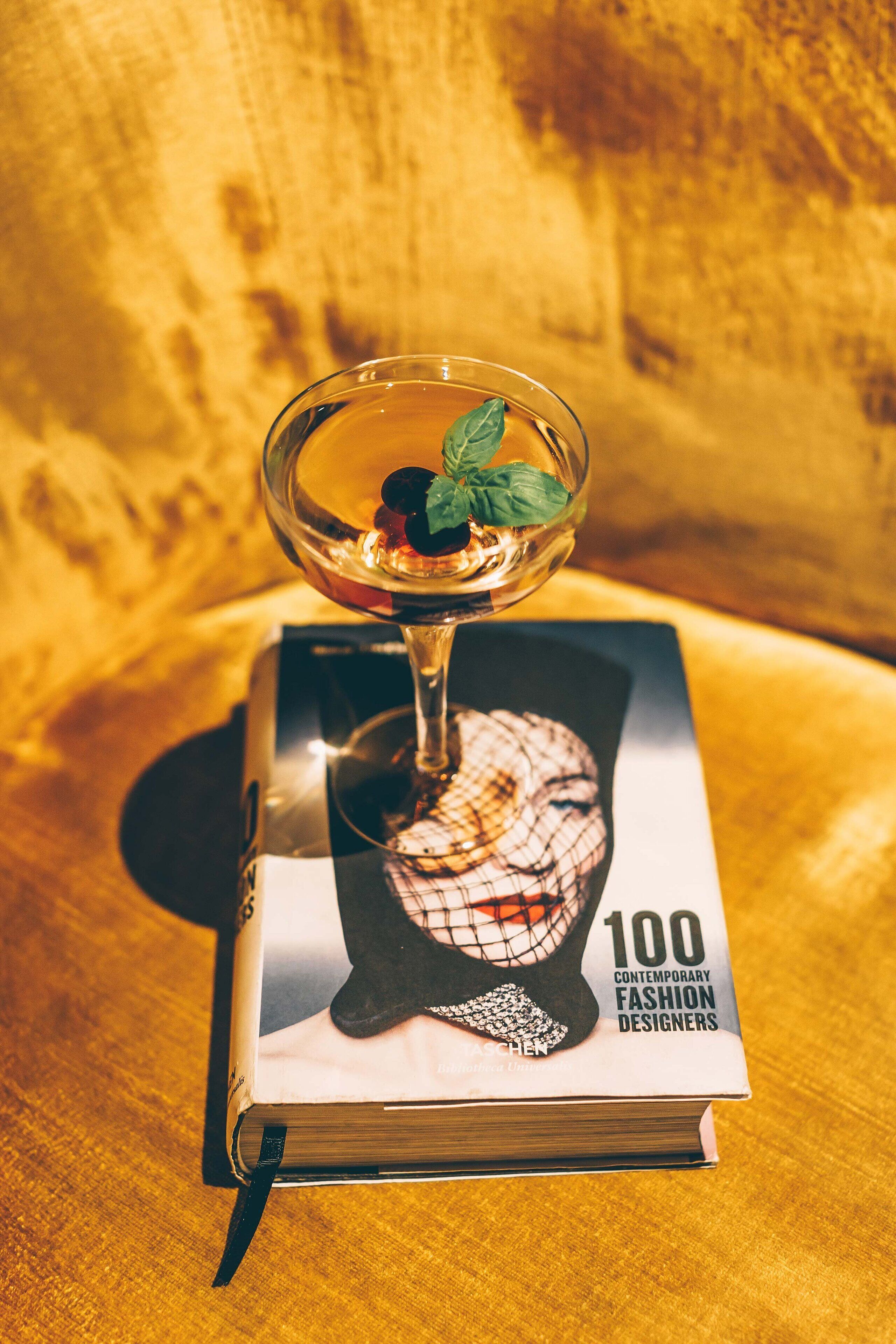 Un libro intitolato "100 Fashion Designer Contemporanei" con un bicchiere da cocktail sopra.