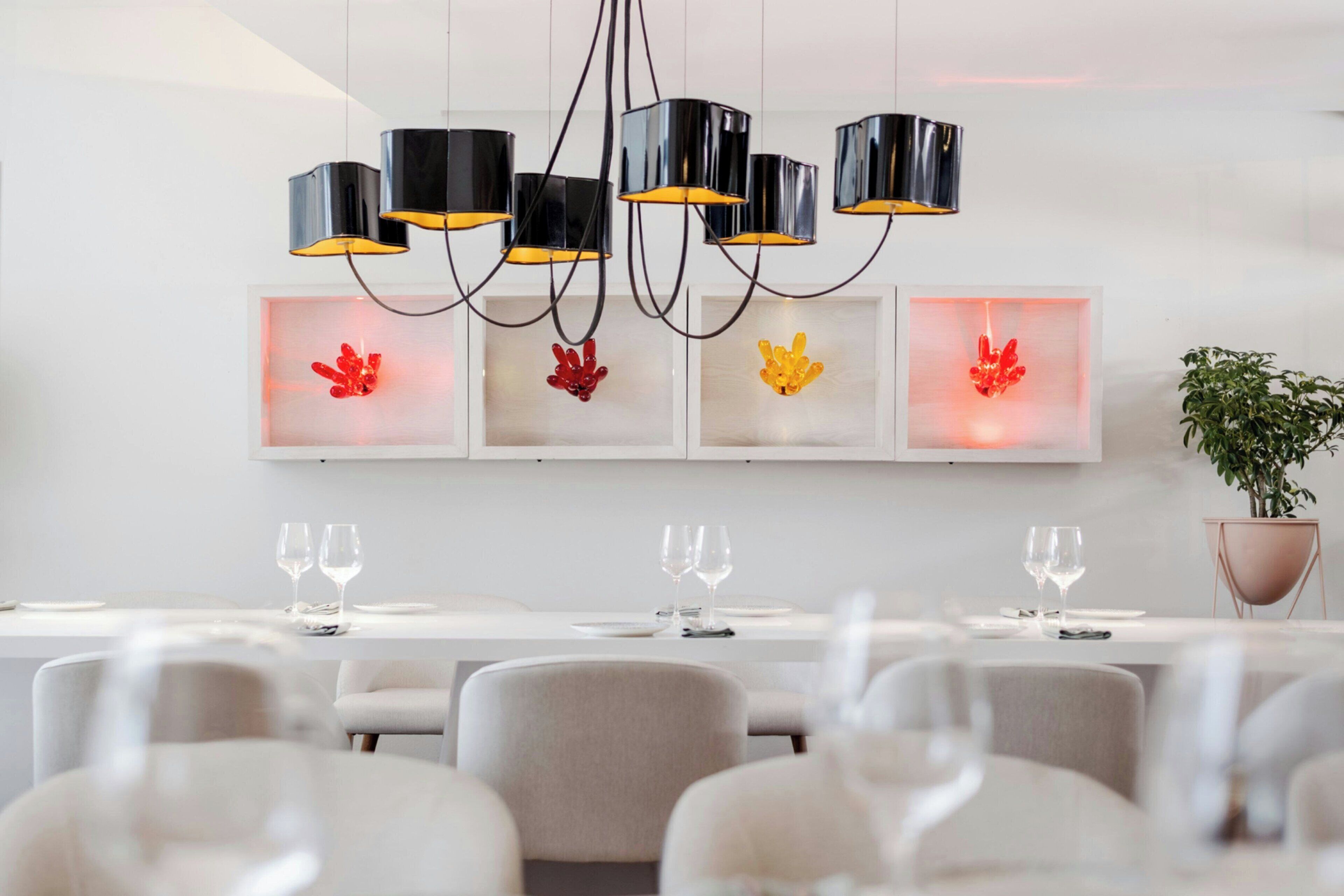 A modern dining area with a long table, multiple chairs, and a chandelier with black and yellow lampshades.