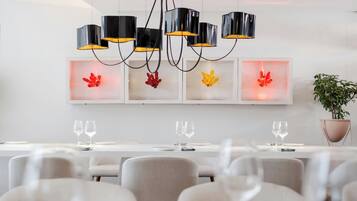 A modern dining area with a long table, multiple chairs, and a chandelier with black and yellow lampshades.