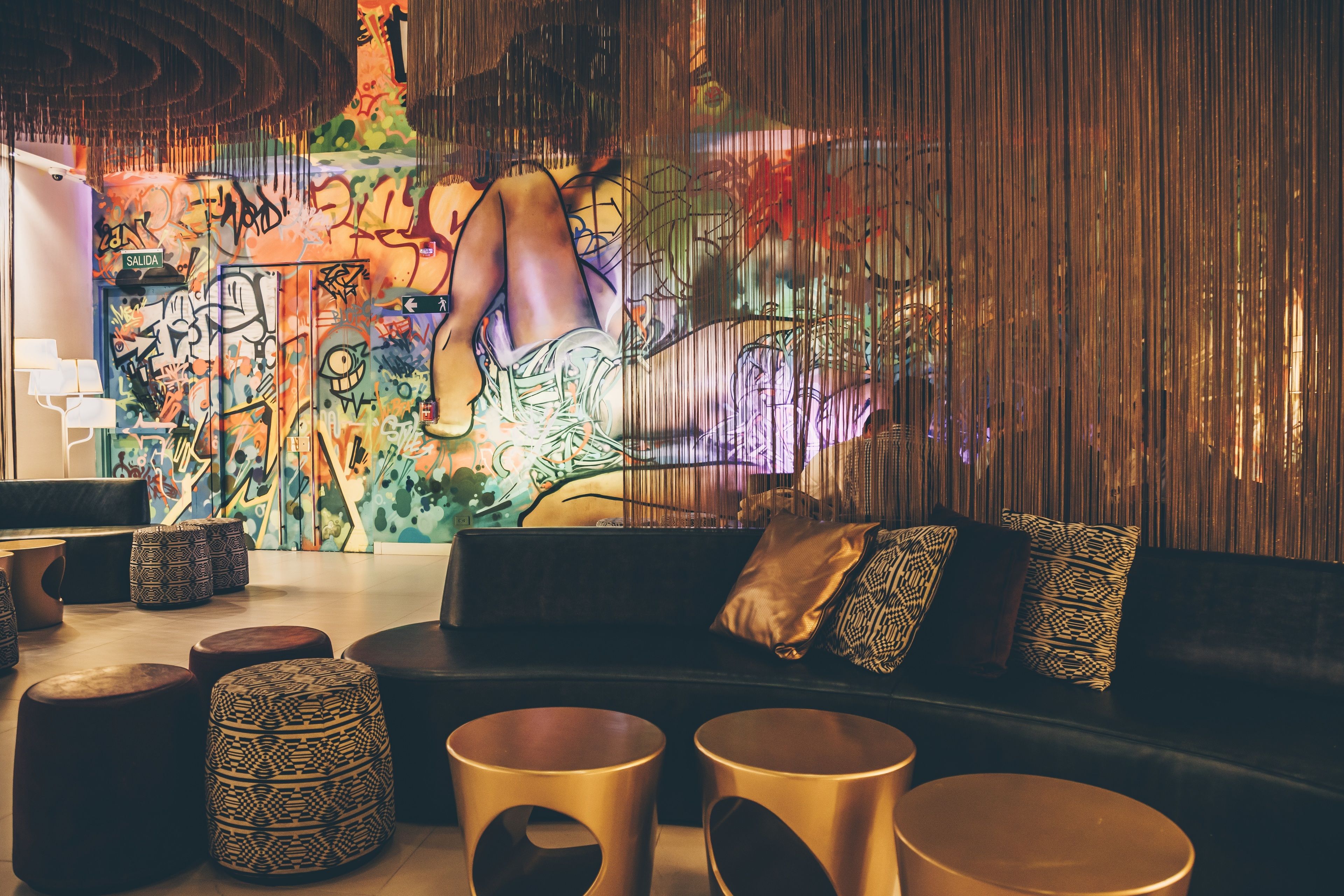 A modern lounge area with a black sofa, patterned ottomans, and a graffiti-covered wall.