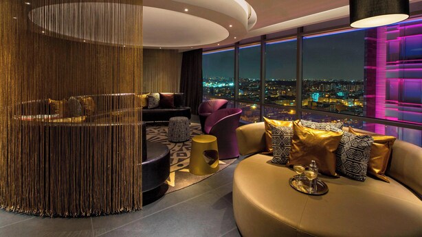 A modern living room with a city view, featuring a curved ceiling, plush seating, and a decorative curtain. - W Bogota (Bogotá)
