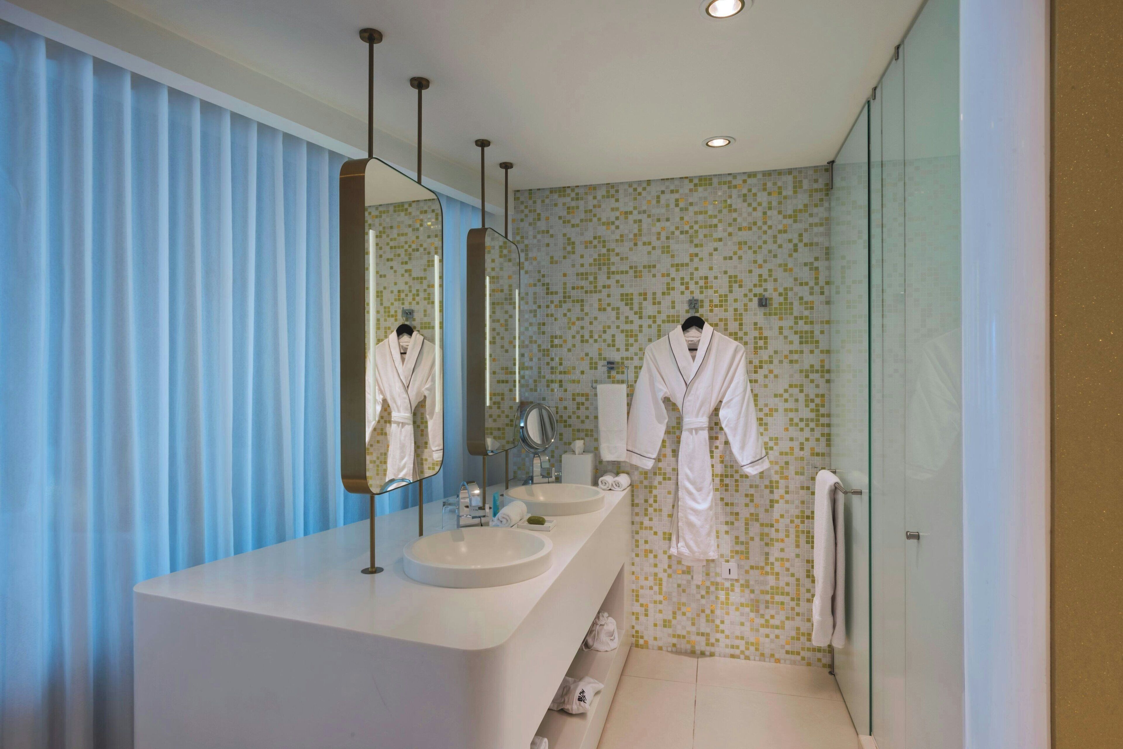 Un baño moderno con un espejo grande, dos lavamanos y una cabina de ducha de vidrio.