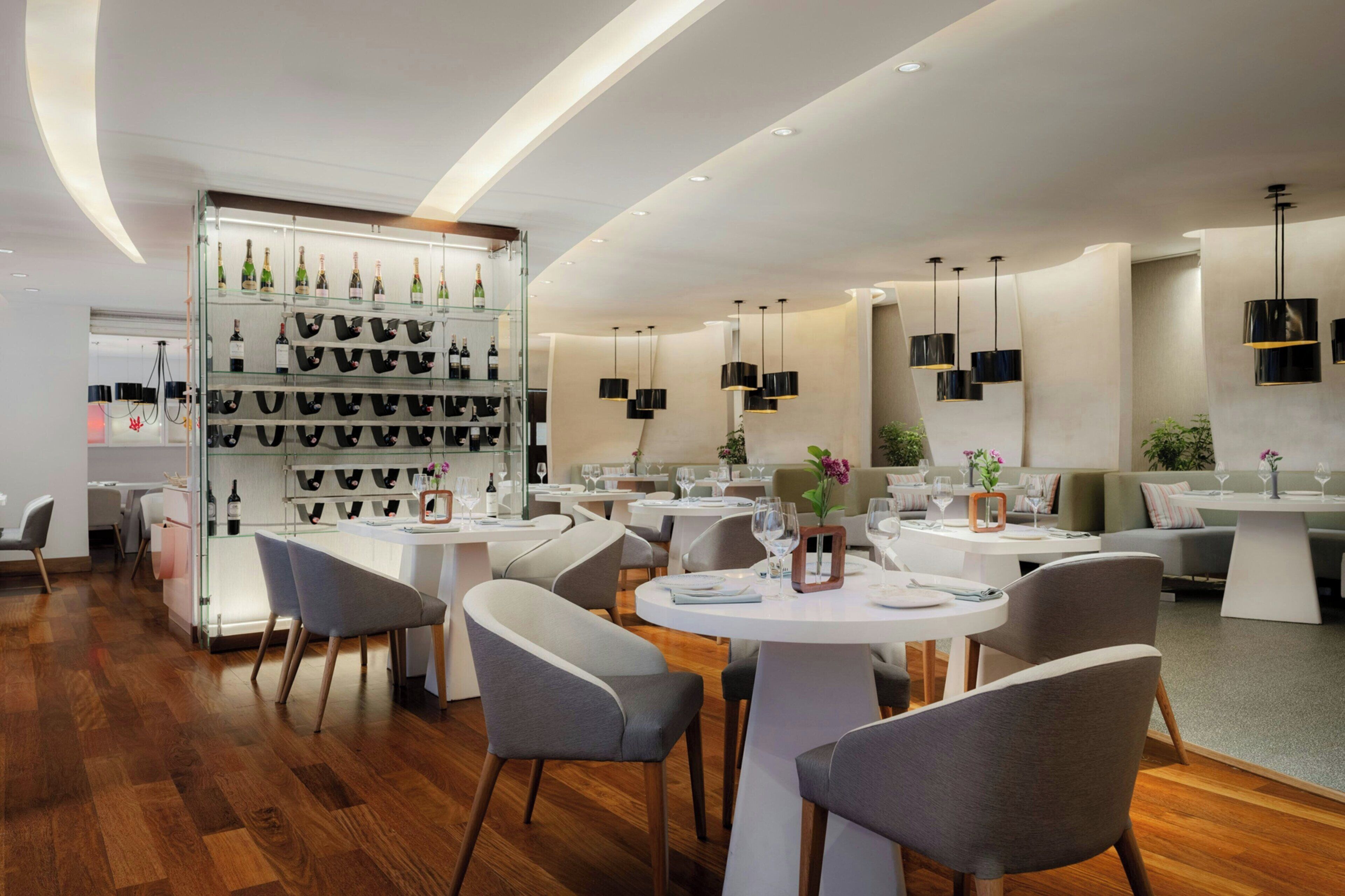 Un restaurante moderno con mesas redondas, sillas grises y una vitrina de vinos.