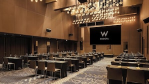 A spacious conference room with multiple tables and chairs, a large screen, and a modern chandelier. - W Bogota (Bogotá)
