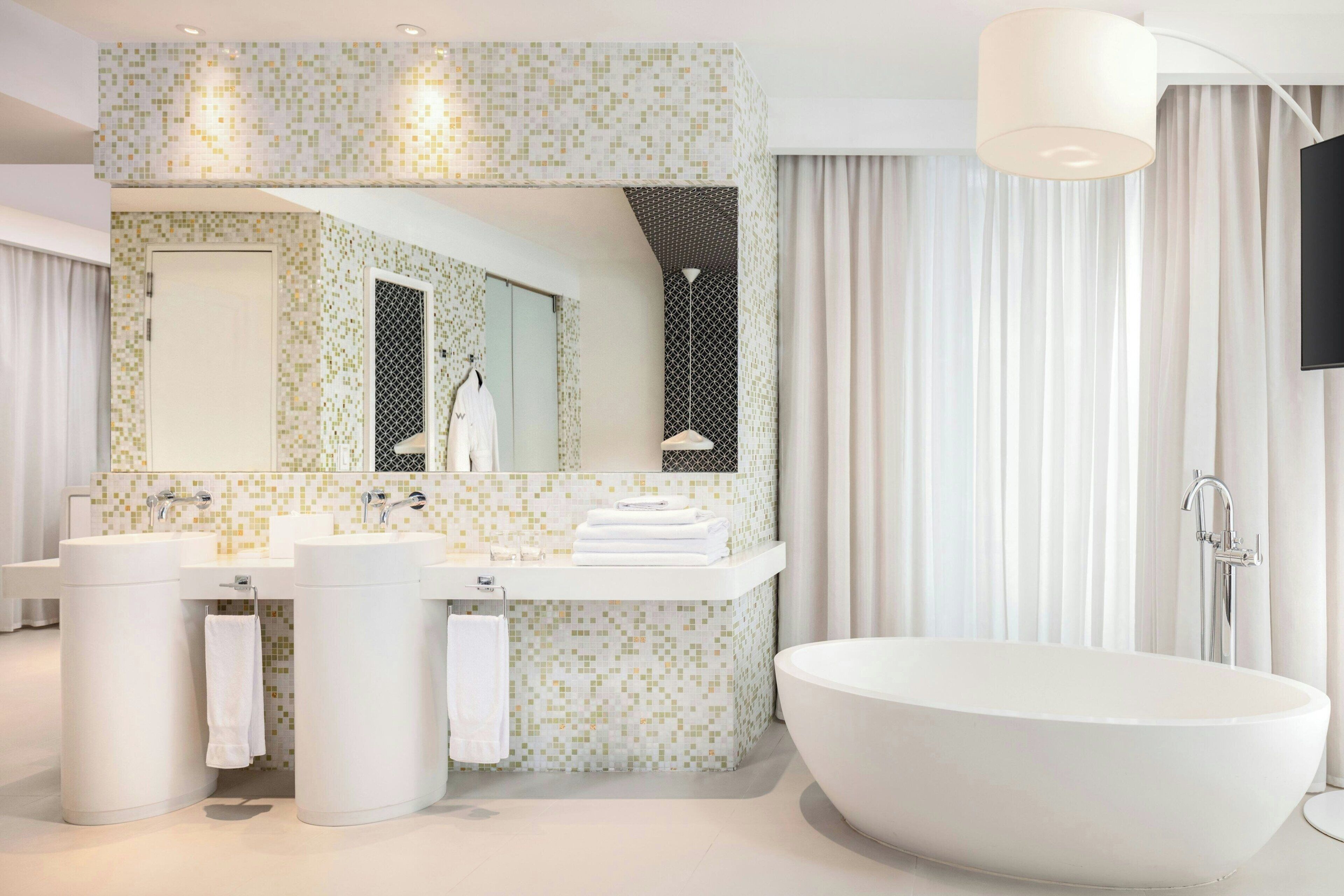 A modern bathroom with a freestanding bathtub, two sinks, and a large mirror.