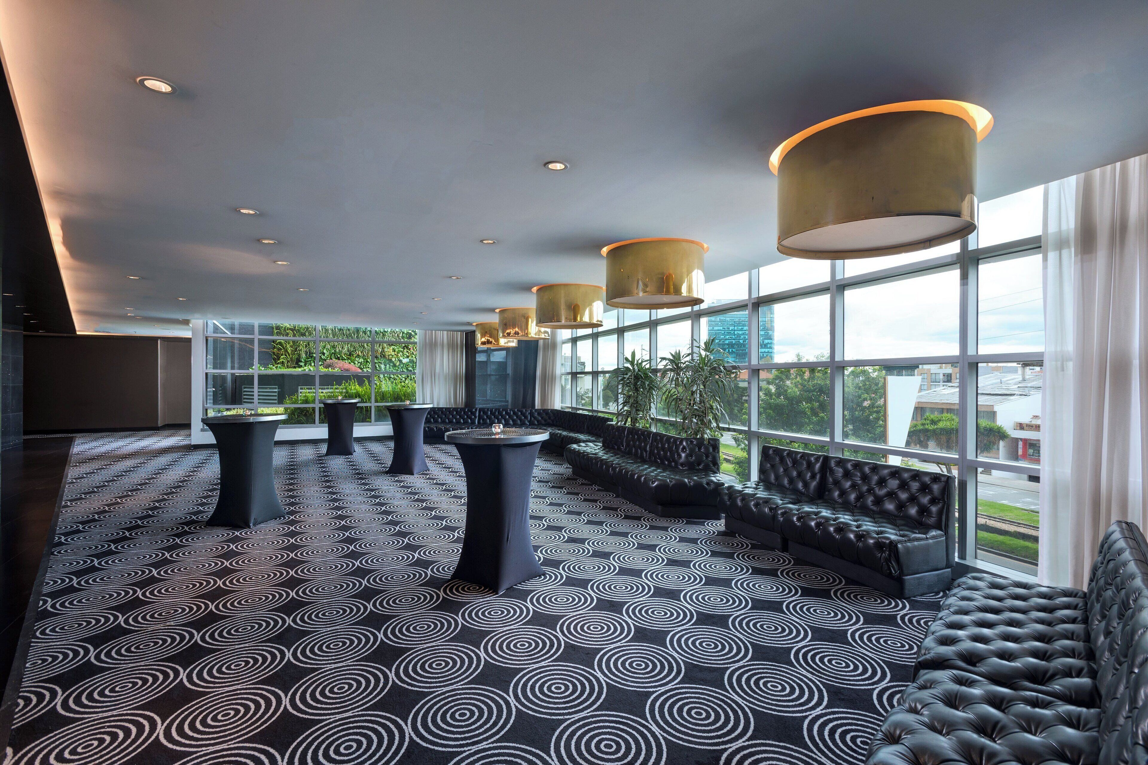 A modern lounge area with a patterned carpet, black sofas, and tall lamps.