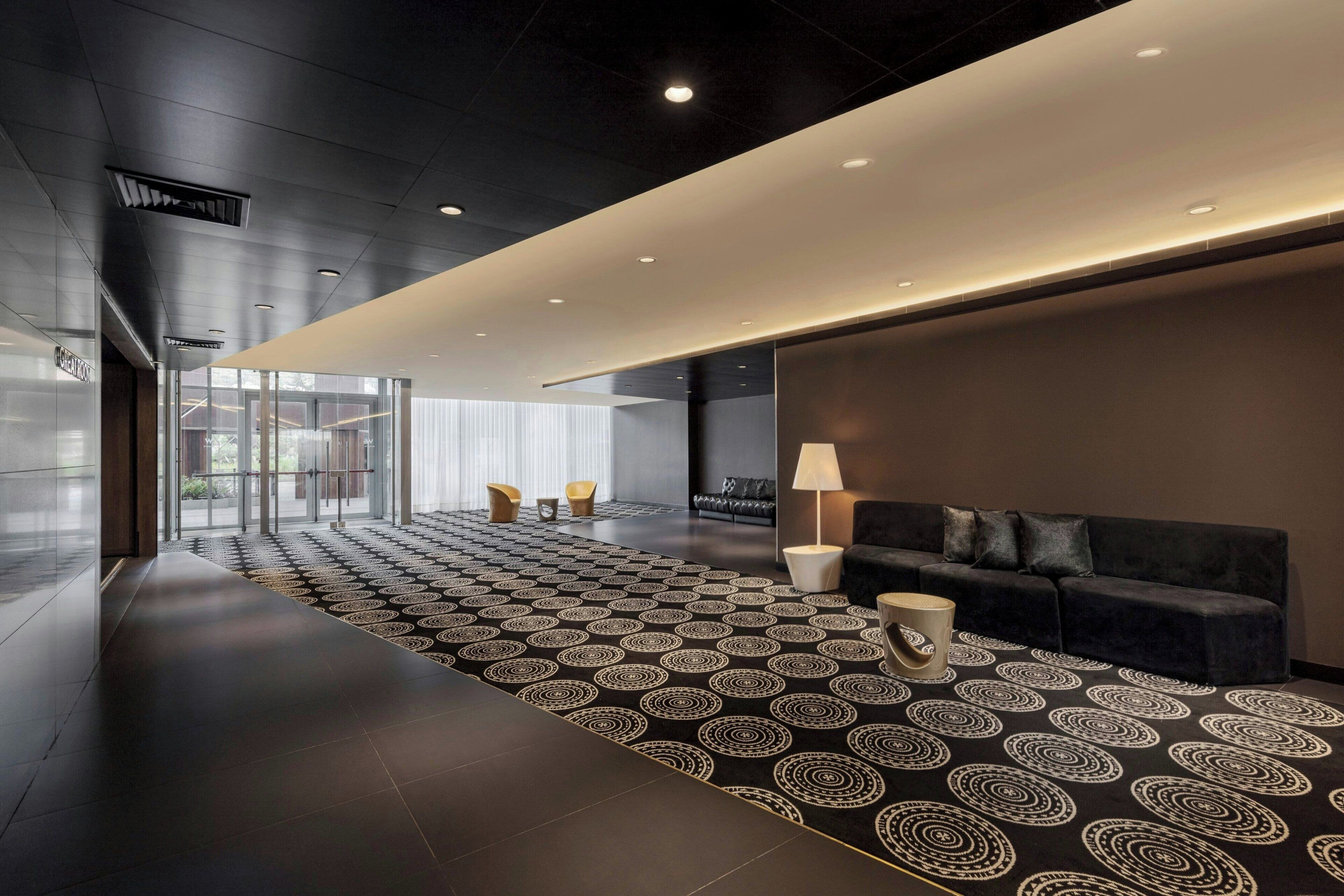 A modern lobby with a patterned carpet, a sofa, and a lamp.