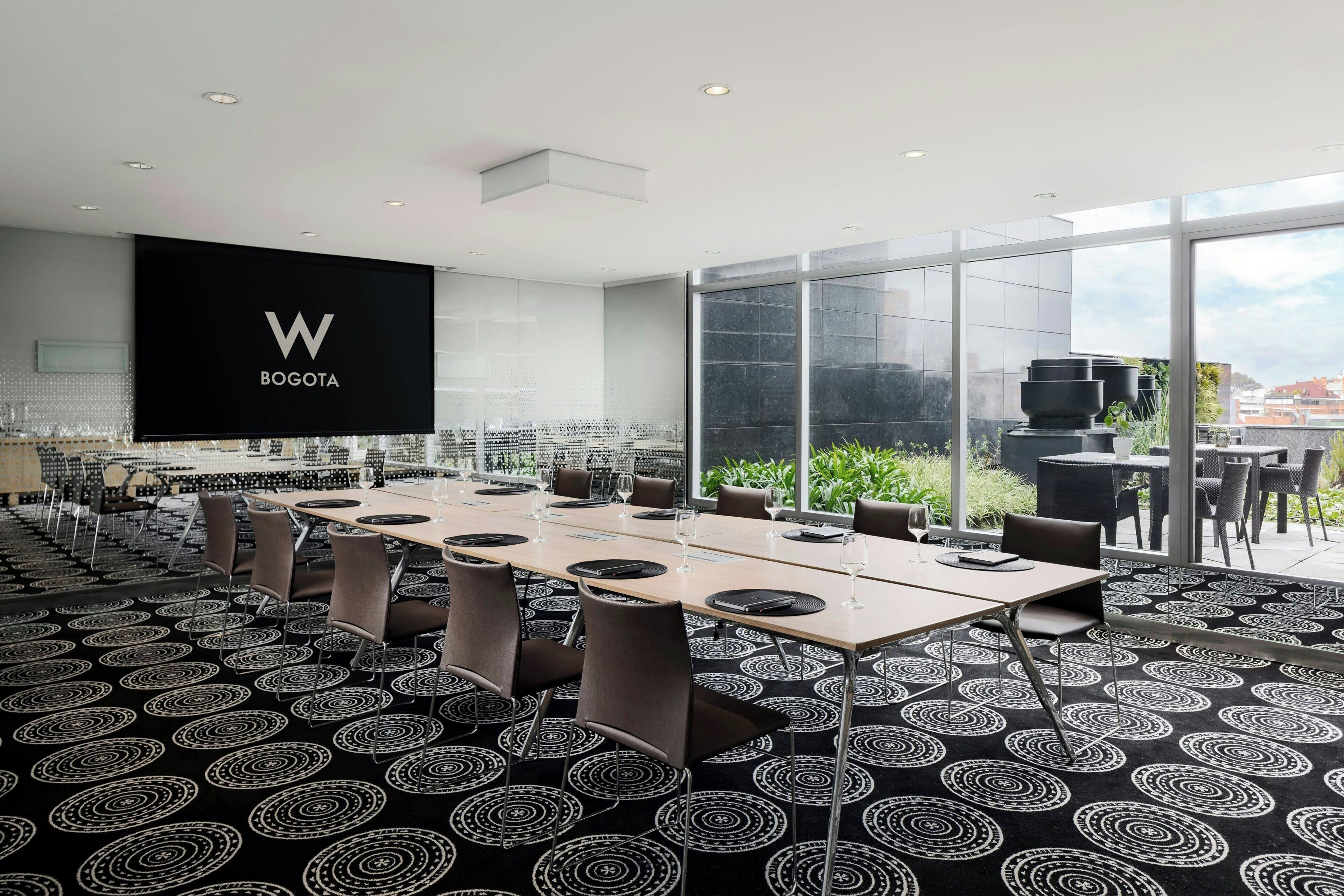A conference room with a large table, chairs, and a screen displaying the logo "W BOGOTA".