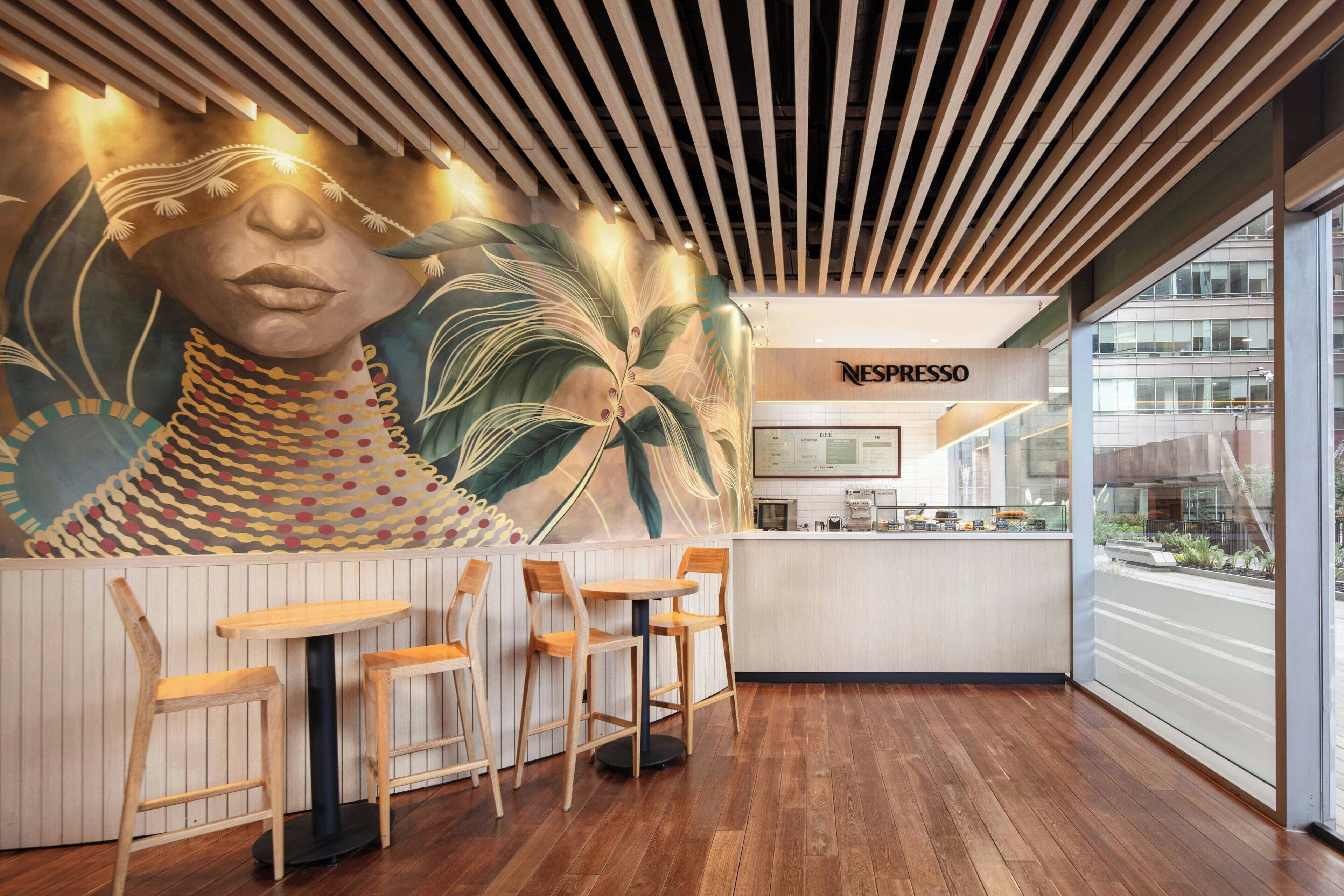 L’intérieur d’un café moderne, avec des meubles en bois, une fresque murale et une vue sur la ville à travers de grandes fenêtres.