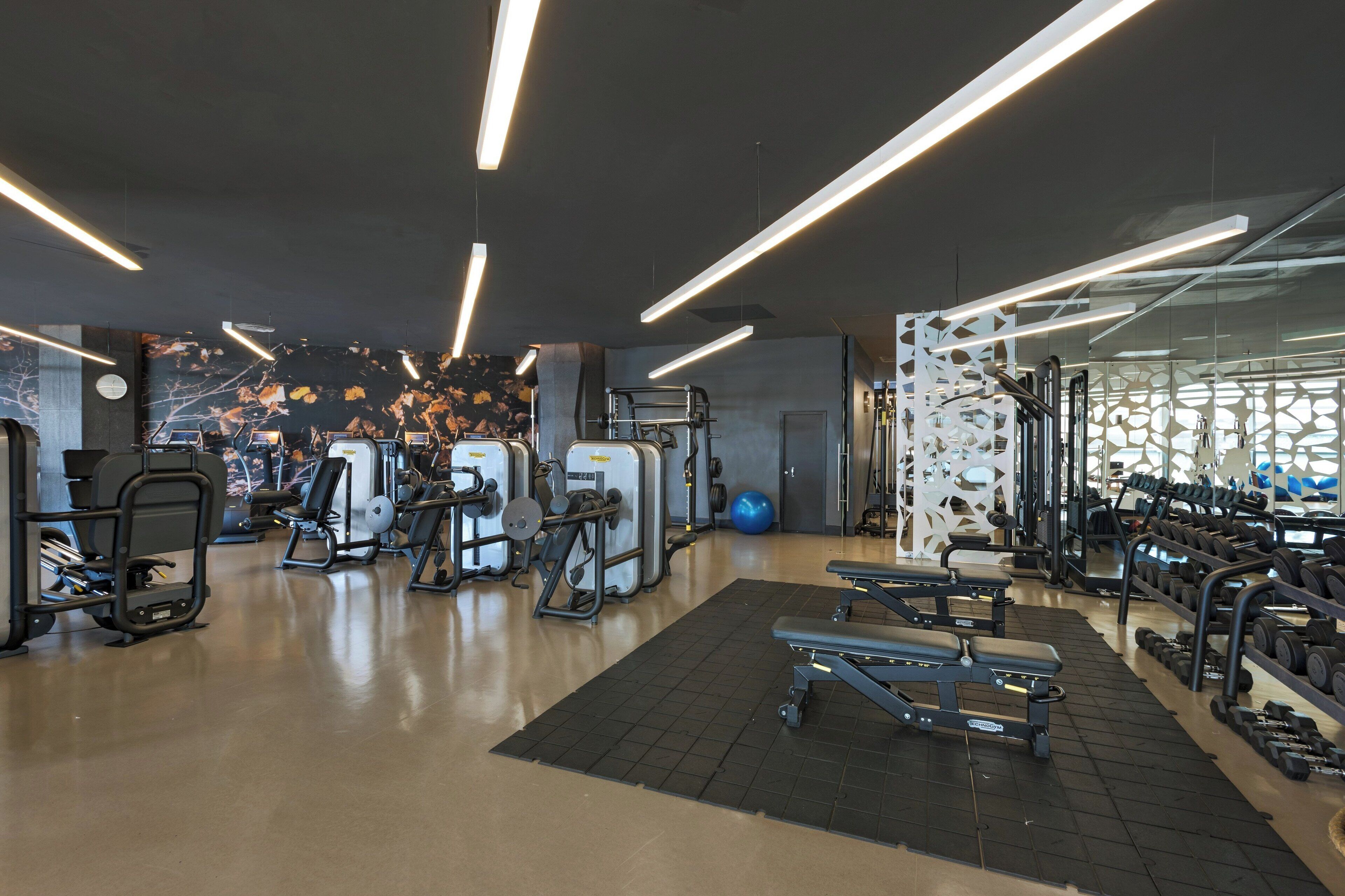 A modern gym with various exercise equipment, a bench, and a wall with a decorative pattern.