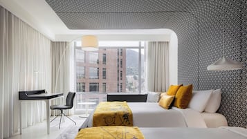 A modern hotel room with two beds, a desk, and a view of the cityscape.