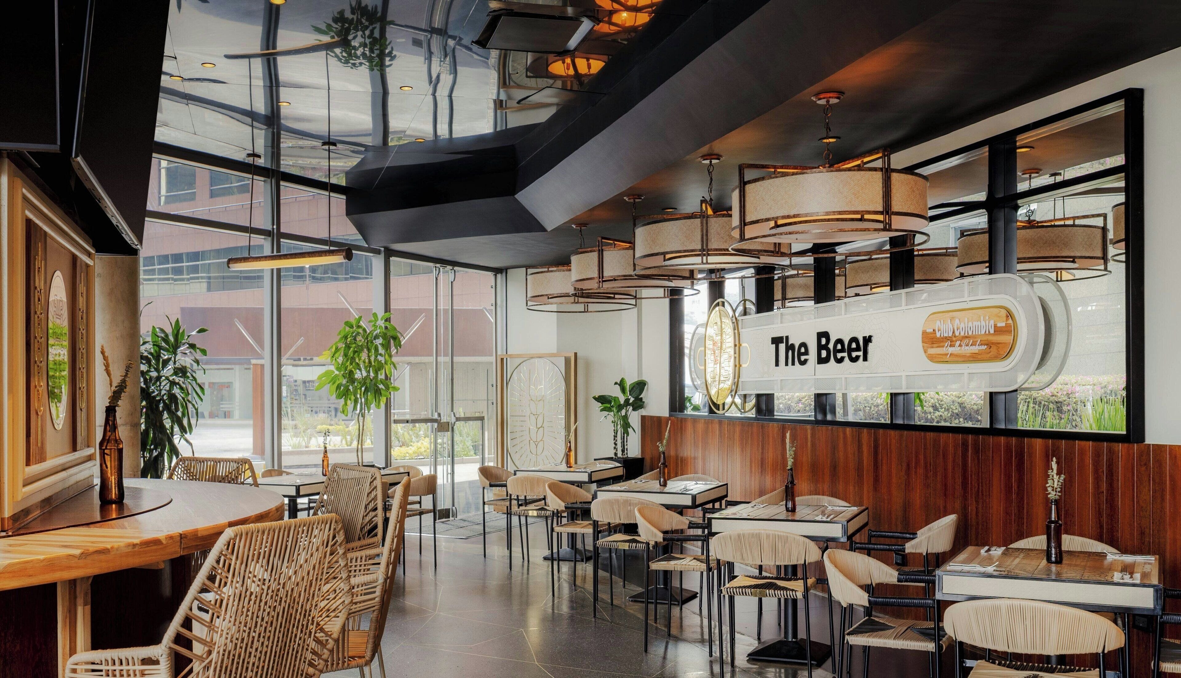 A modern restaurant interior with high ceilings, large windows, and a variety of seating arrangements including tables and chairs.