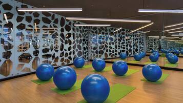 Une salle de sport avec des ballons d’exercice sur des tapis verts, un plancher en bois et un mur orné de motifs géométriques découpés.