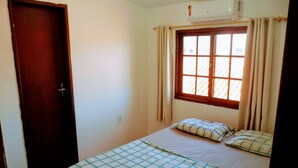 A bedroom with a bed, a window with curtains, a door, and an air conditioner. - Ingleses Residence (Florianópolis)