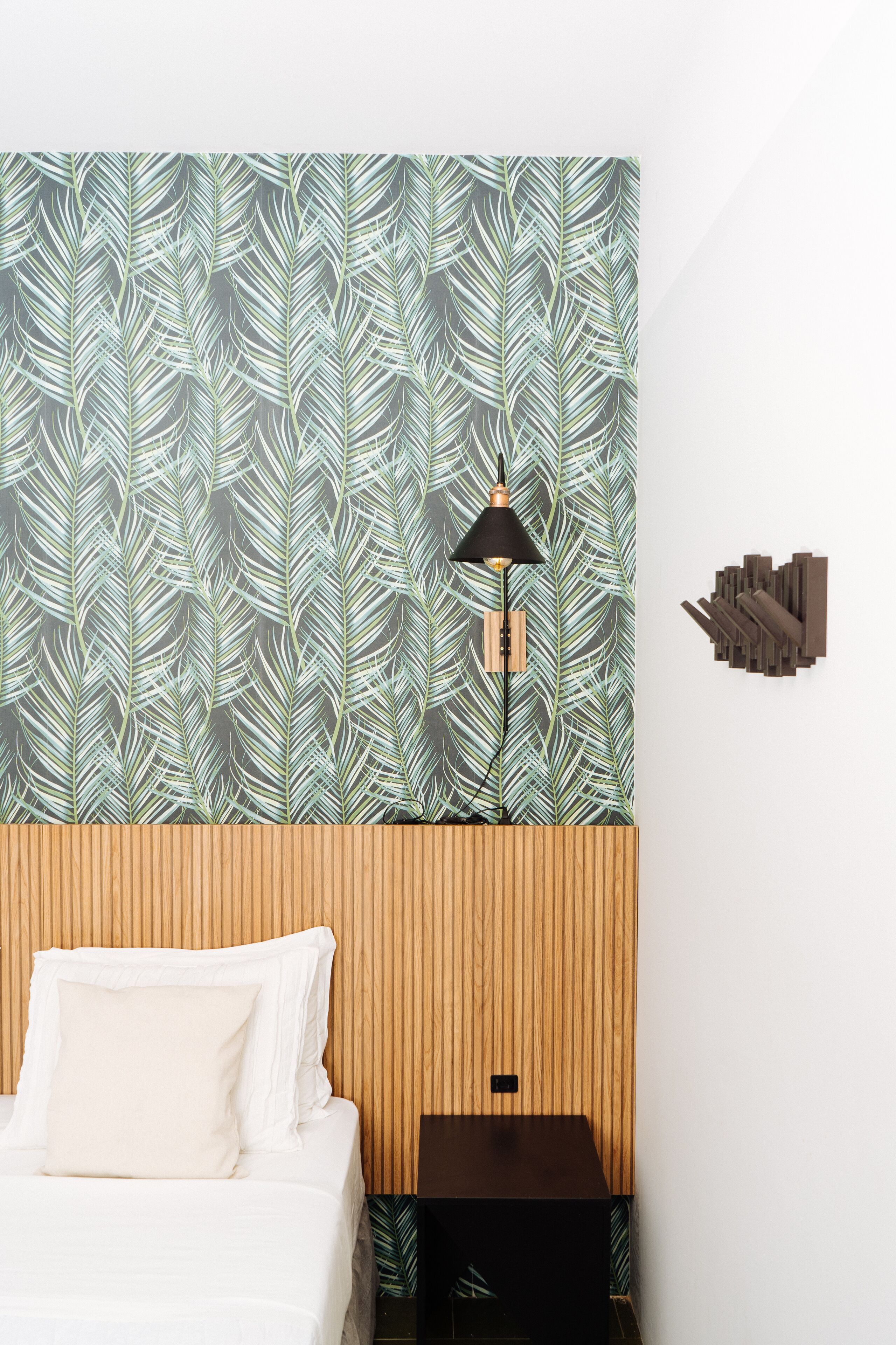 A bedroom with a patterned wallpaper, a bedside lamp, a wooden headboard, and a nightstand.