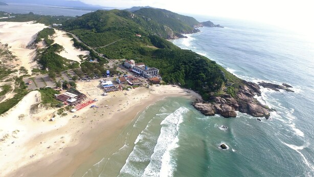 Una vista aerea di una zona costiera con spiaggia, un piccolo paese con edifici e montagne sullo sfondo.