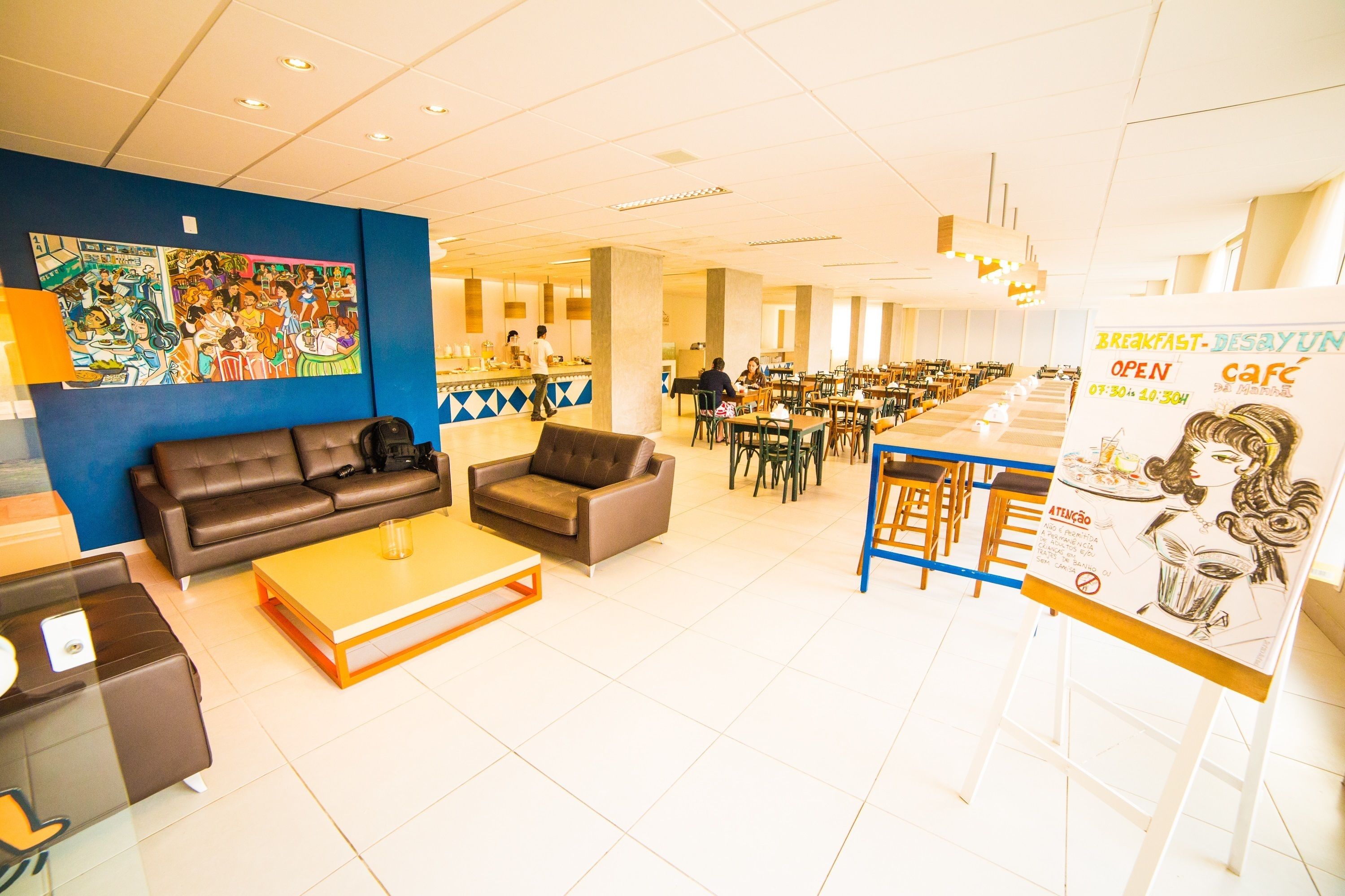 Un moderno vestíbulo de hotel con zona de comedor, sofás y un mural colorido en la pared.