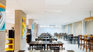 Un'ampia sala da pranzo con diversi tavoli e sedie, un carrello giallo e opere d'arte alle pareti.