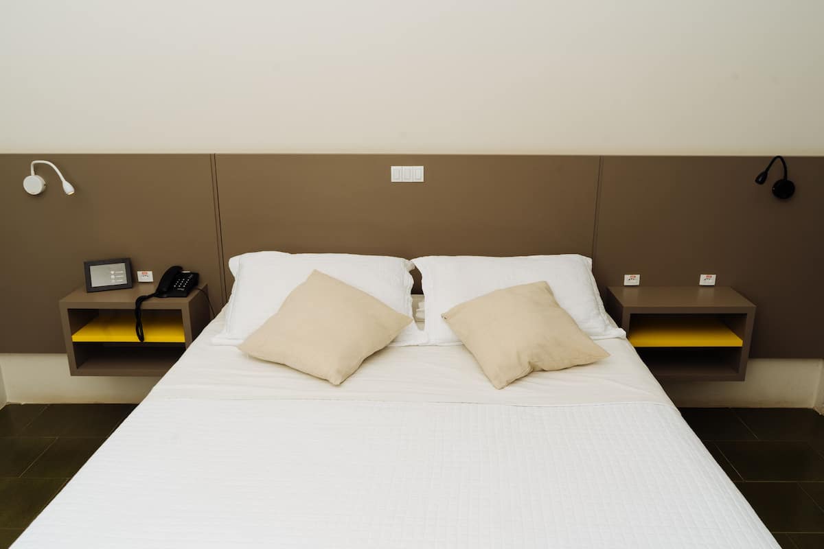 A hotel room with a bed, two bedside tables, a phone, and headphones on the wall.