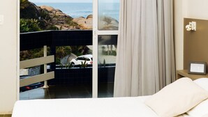 Una camera d'albergo con un'ampia porta-finestra che si apre su un balcone con vista sull'oceano e sul paesaggio roccioso.