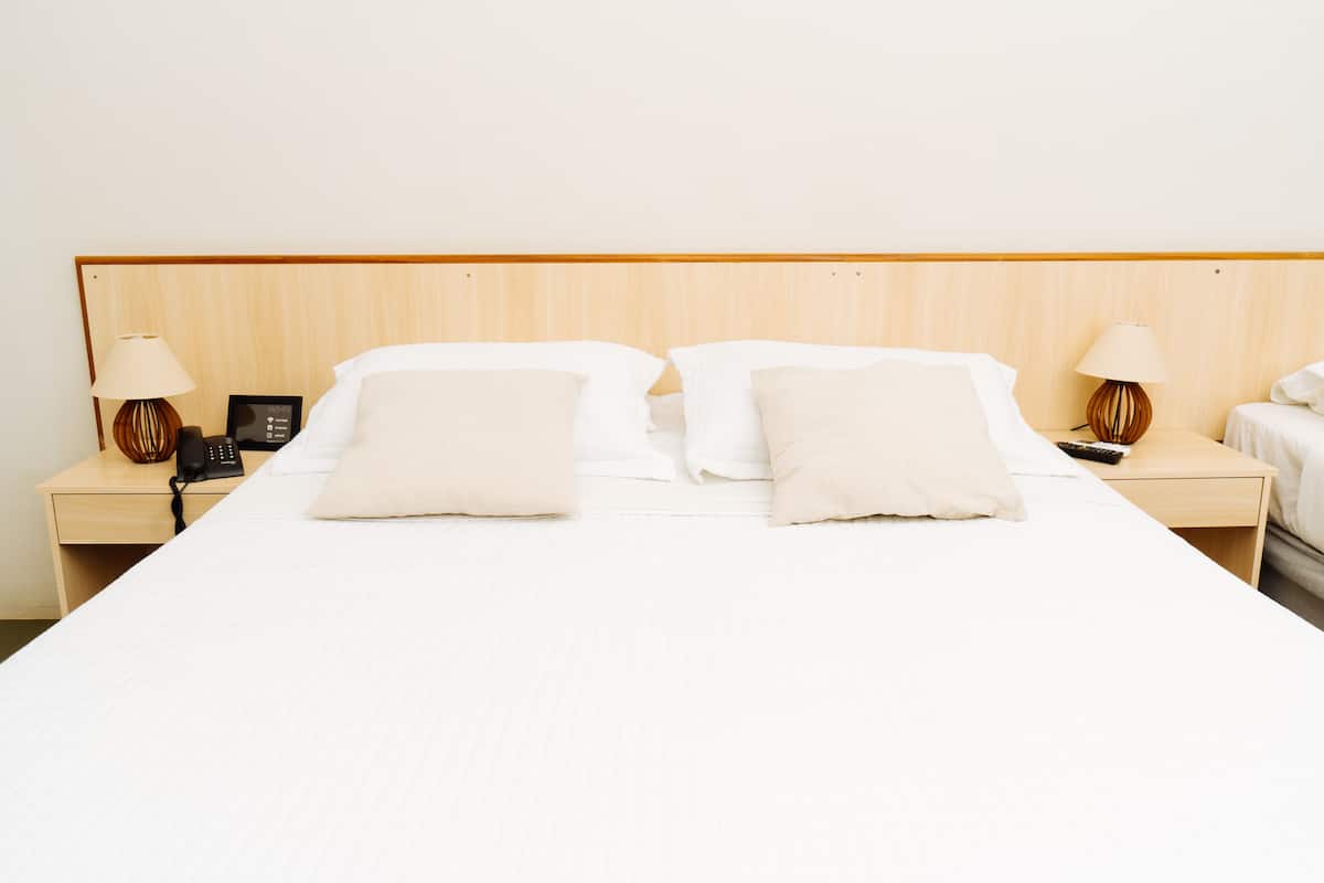 A hotel room with a wooden headboard, two bedside tables, a bed with white linens, and two lamps on each side.
