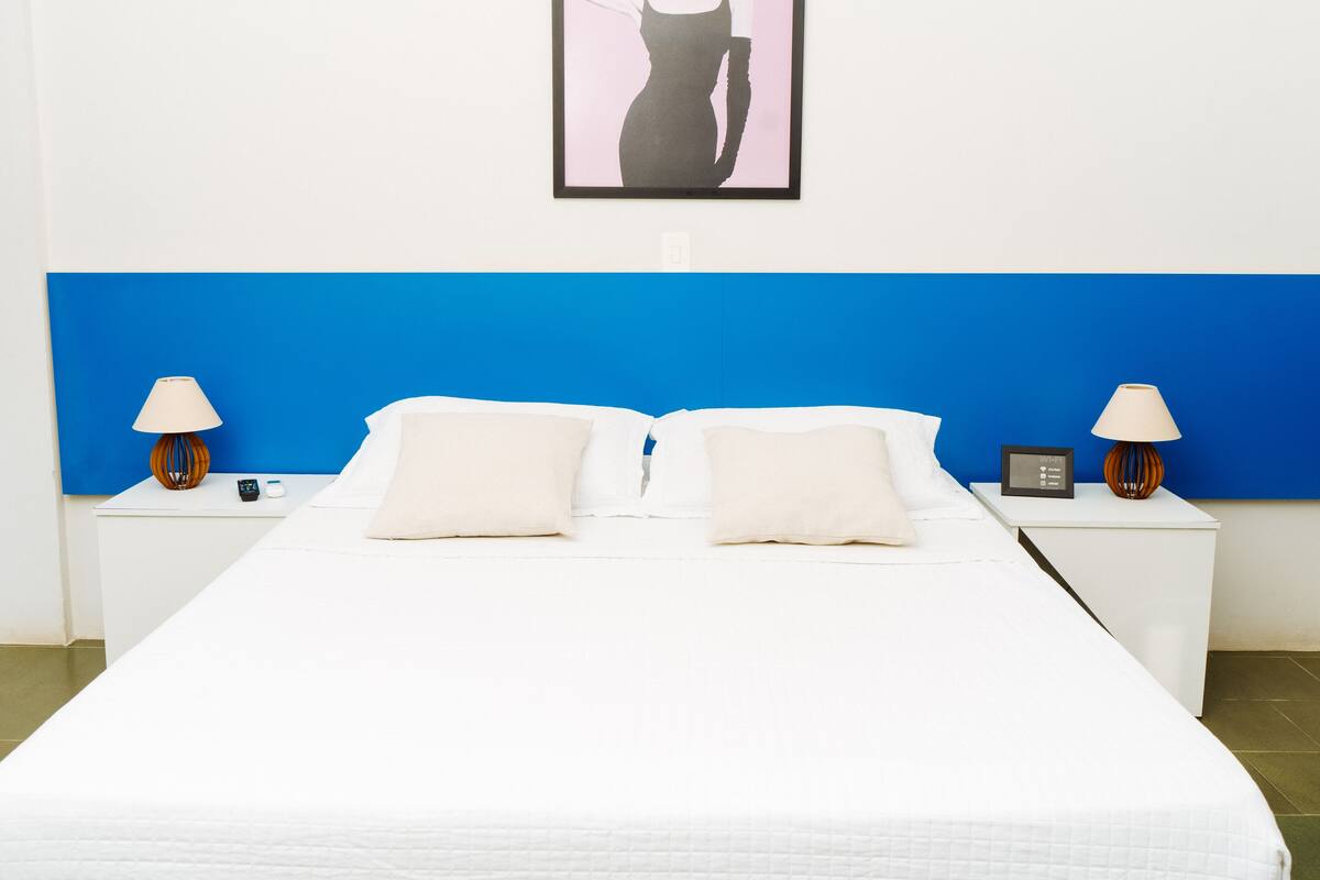 A neatly made bed with white linens, two bedside tables with lamps, and a framed picture on the wall.