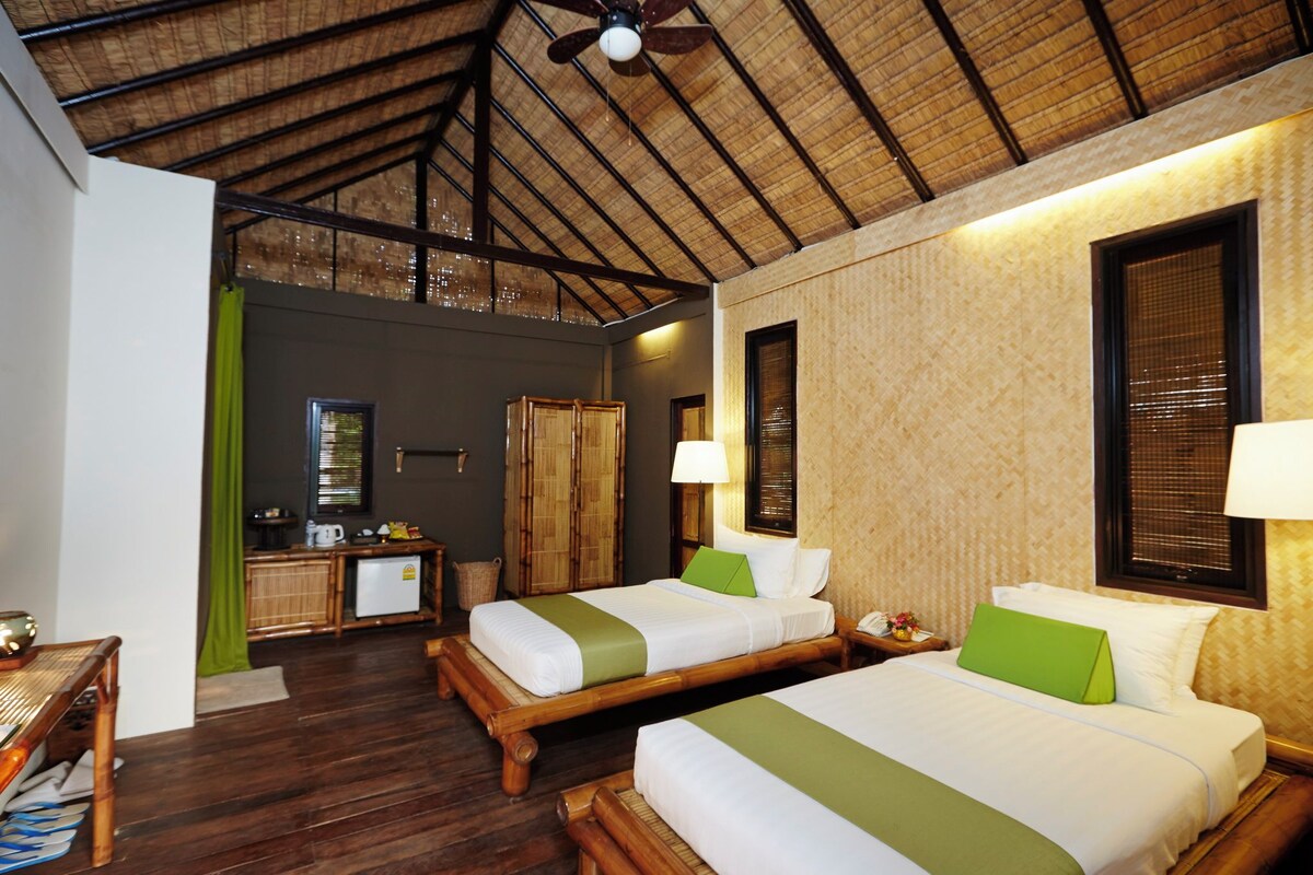 A hotel room with two beds, a small kitchenette, and a ceiling fan.