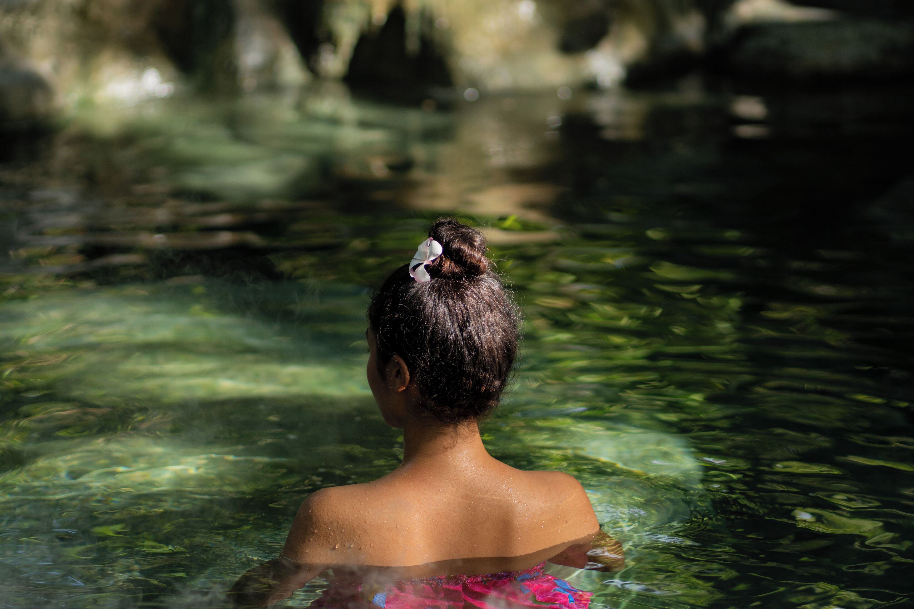 A person in a natural setting with clear water, rocks, and greenery.