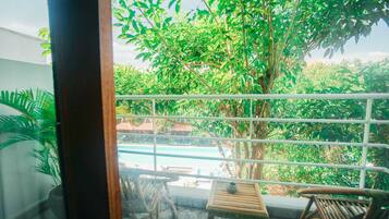 Un balcón con vista a una piscina, rodeado de abundante vegetación y un árbol grande.