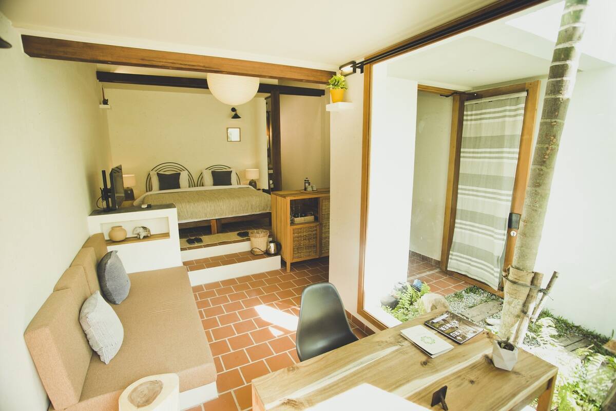 Een gezellige kamer met een bed, een houten bureau, een stoel en een klein balkon met uitzicht.