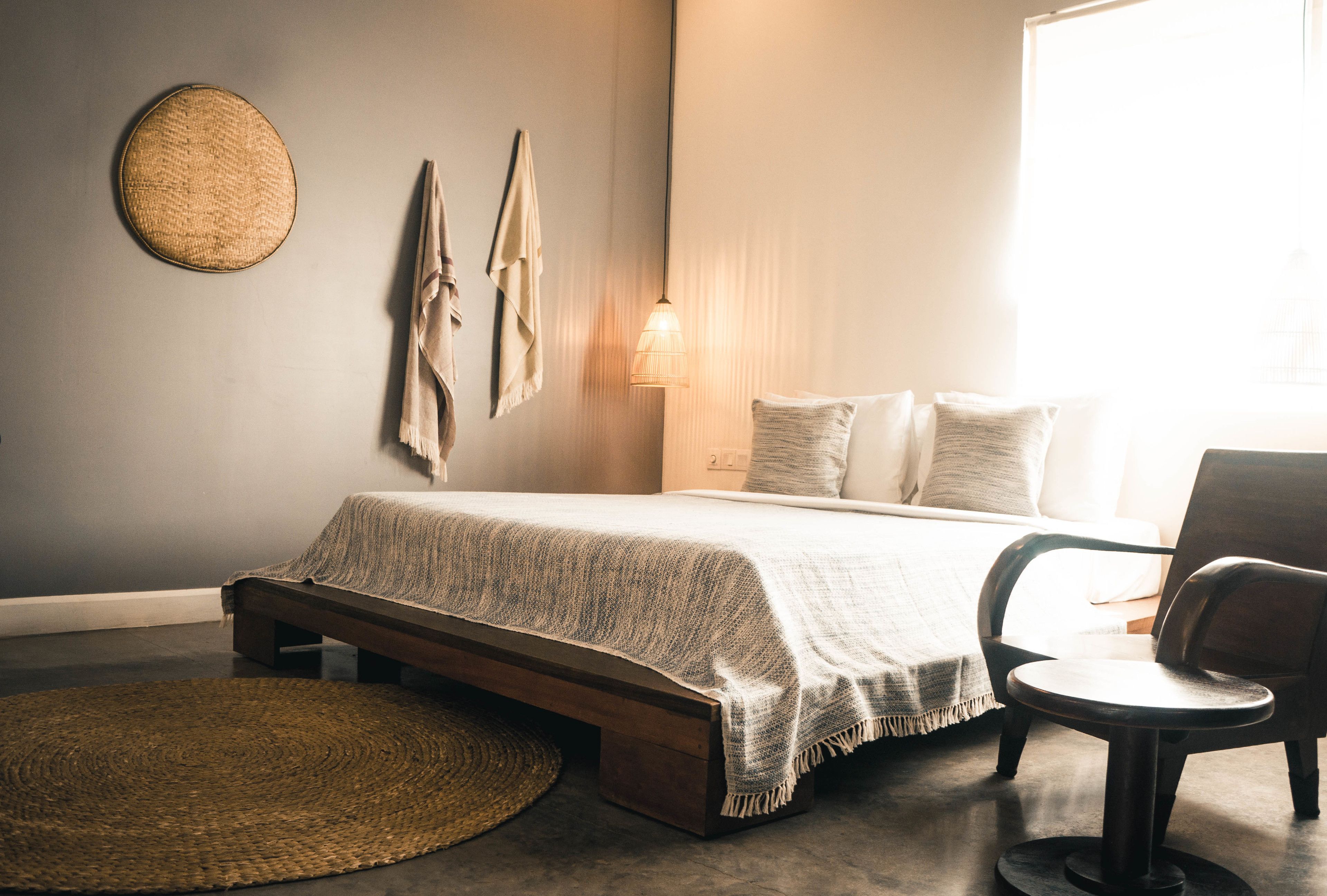 Un dormitorio con una cama, una silla, un tapiz tejido y una lámpara fijada a la pared.