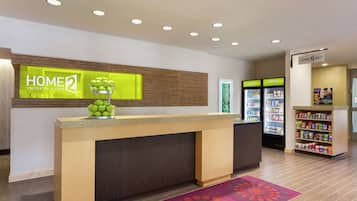 Ein Hotel-Empfangsbereich mit einer Rezeption, einer Obstschale, einem Kühlschrank und einer Snackbar.